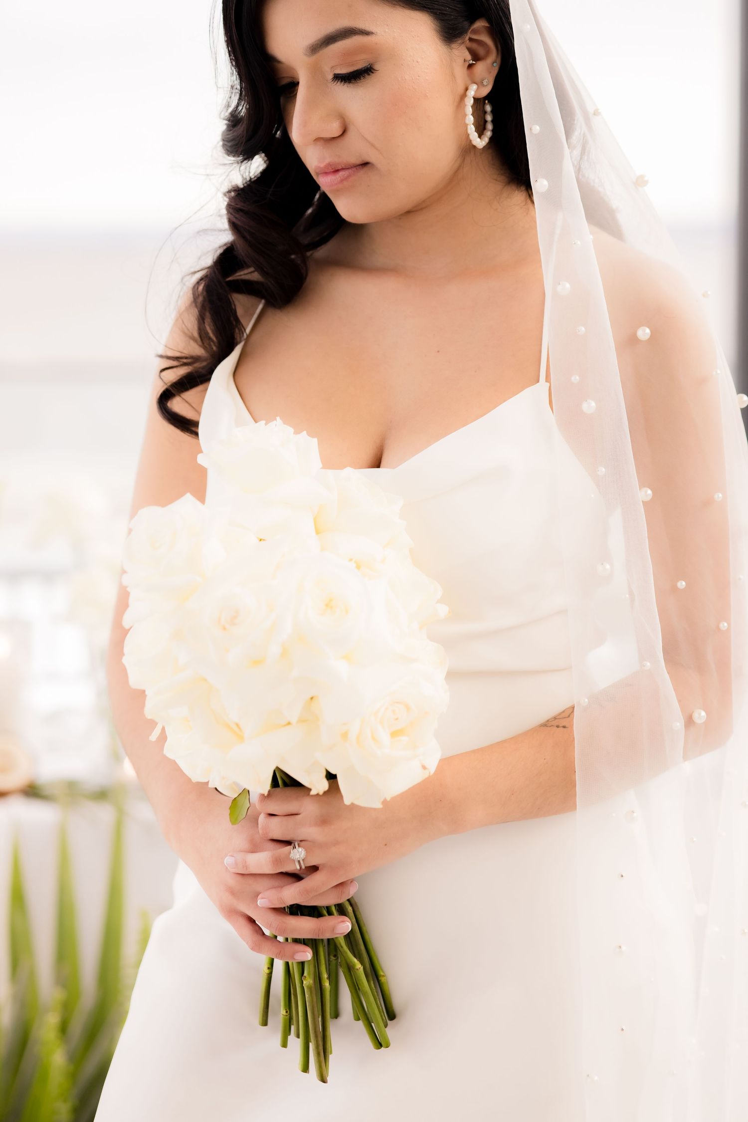 Close-up of bride holding white bouquet wearing veil and elegant spaghetti strap dress.