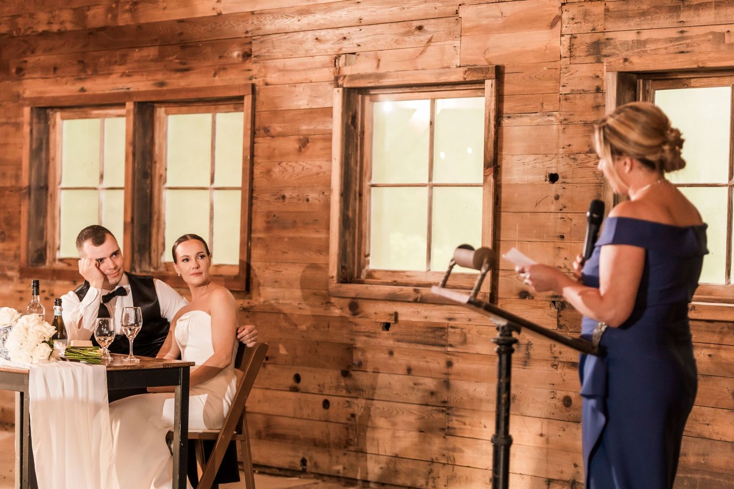 A rustic barn wedding venue interior features exposed wooden walls and large windows creating natural lighting.