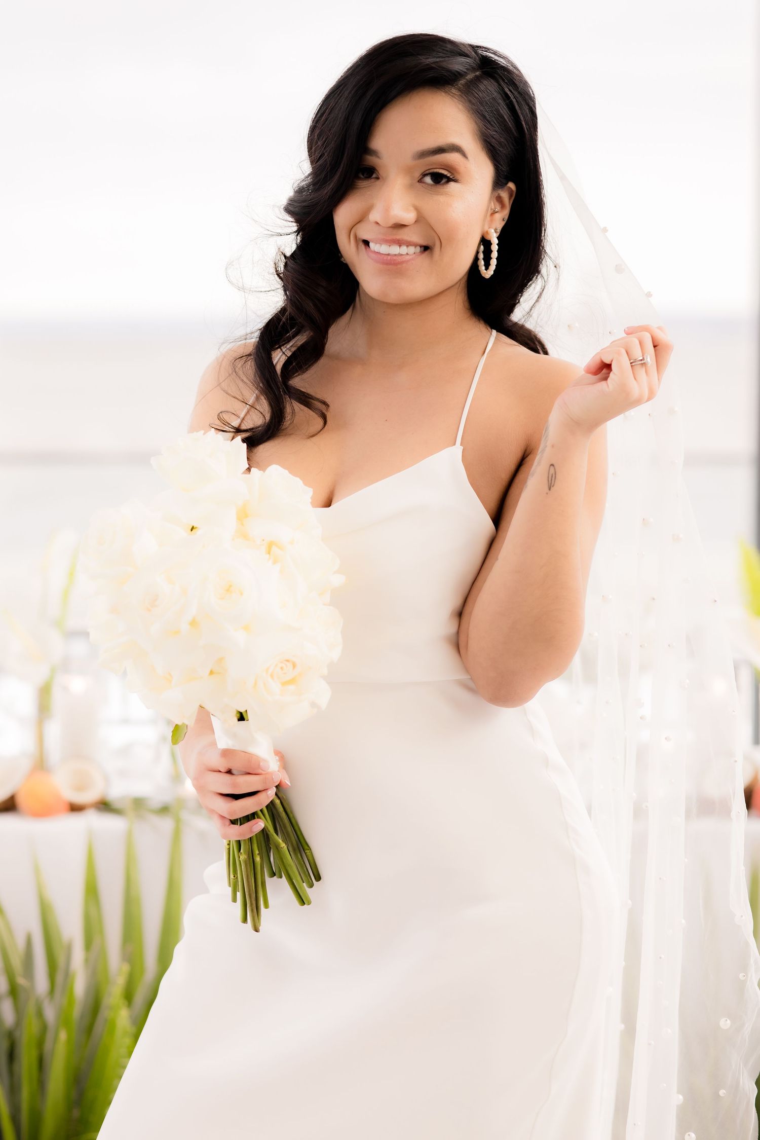 Bride holding white floral bouquet in sleek wedding dress at modern venue.
