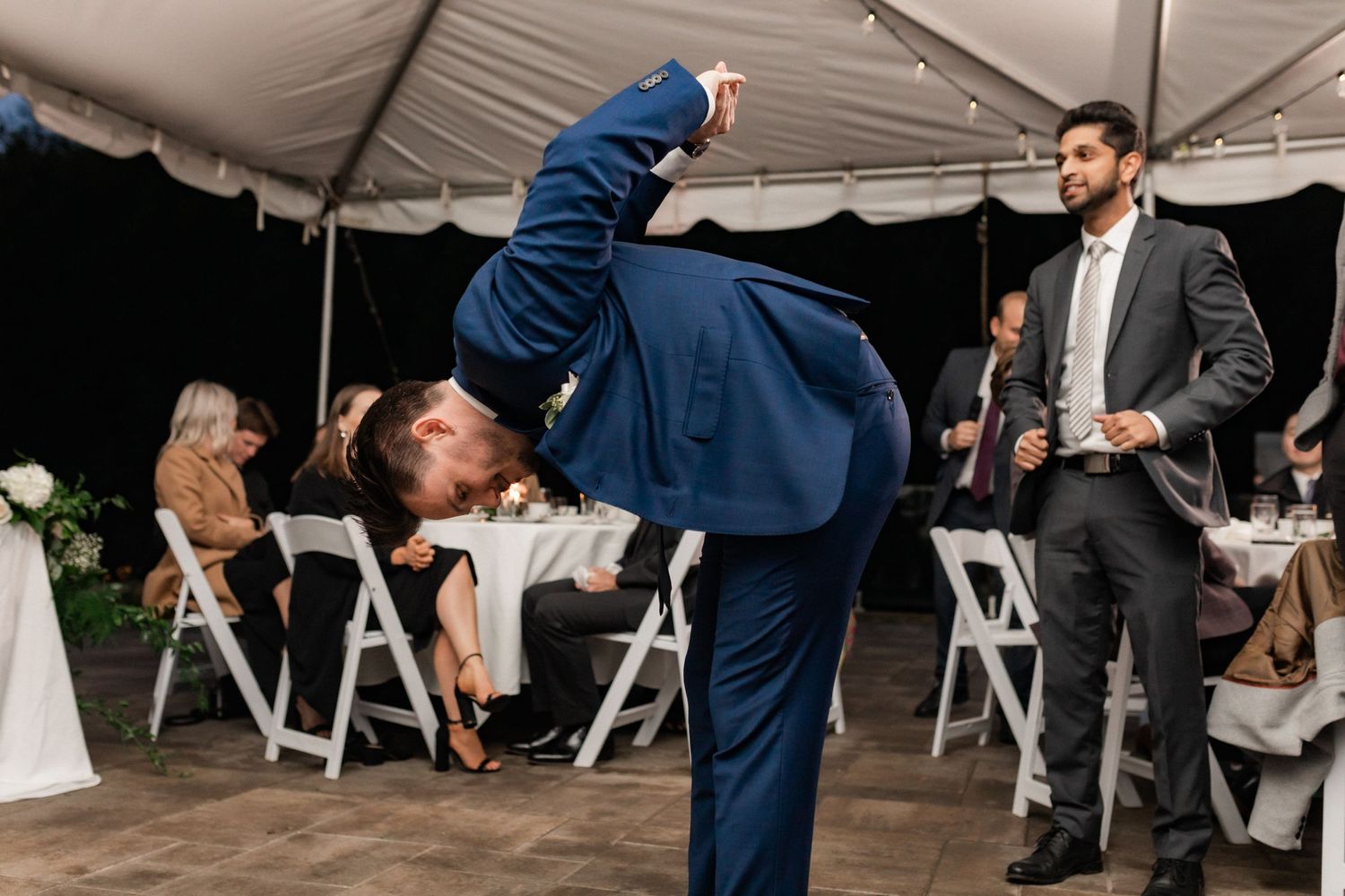 Fun moment at a wedding reception as guests dance under a white tent.