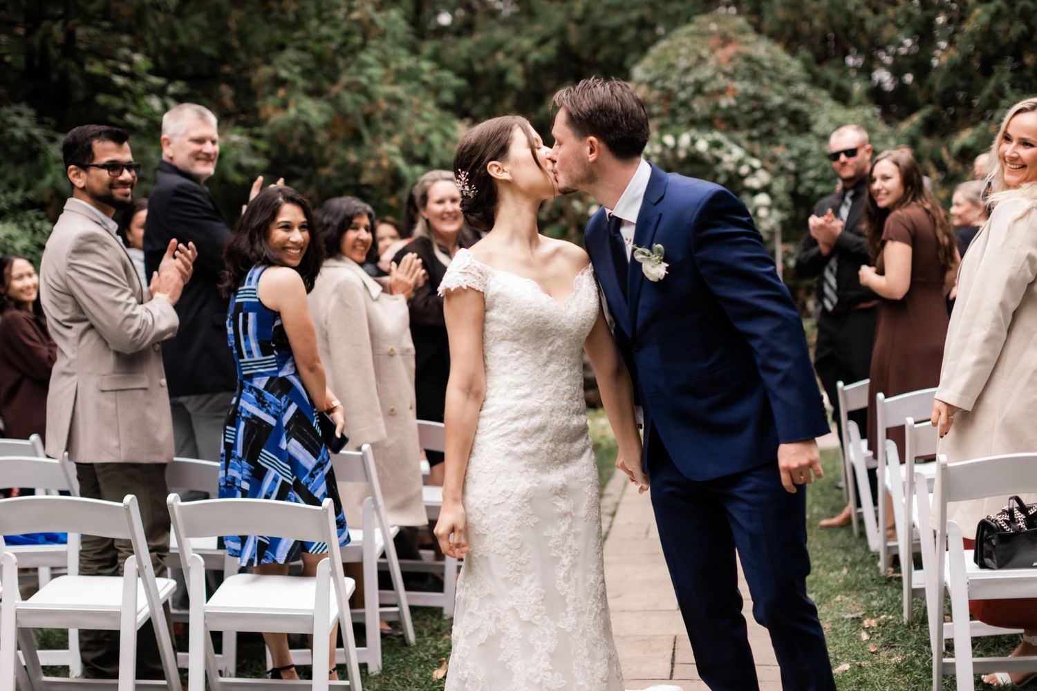 A romantic moment shared between newlyweds with wedding guests in the background.