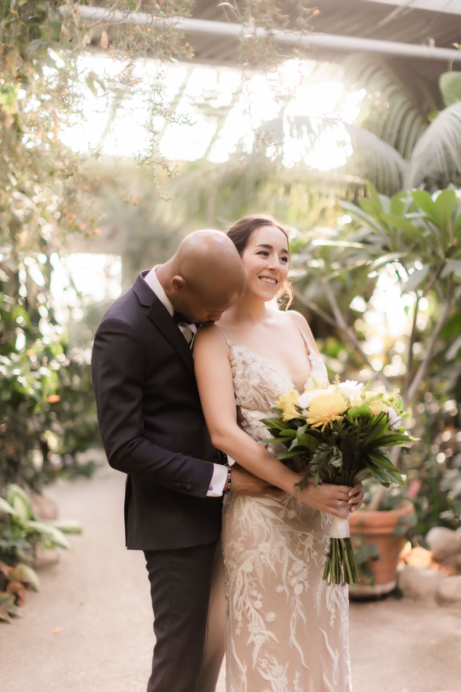 A romantic wedding portrait in a conservatory with tropical plants and yellow flowers.