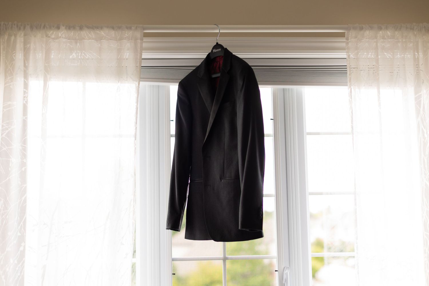 Black suit jacket hanging in window with sheer white curtains.
