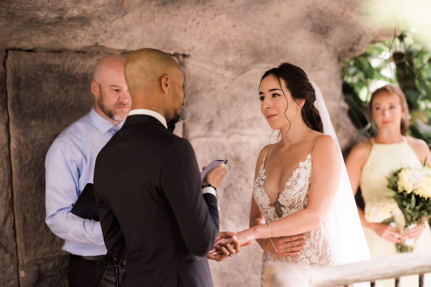 Couple exchanges rings during wedding ceremony under stone archway.