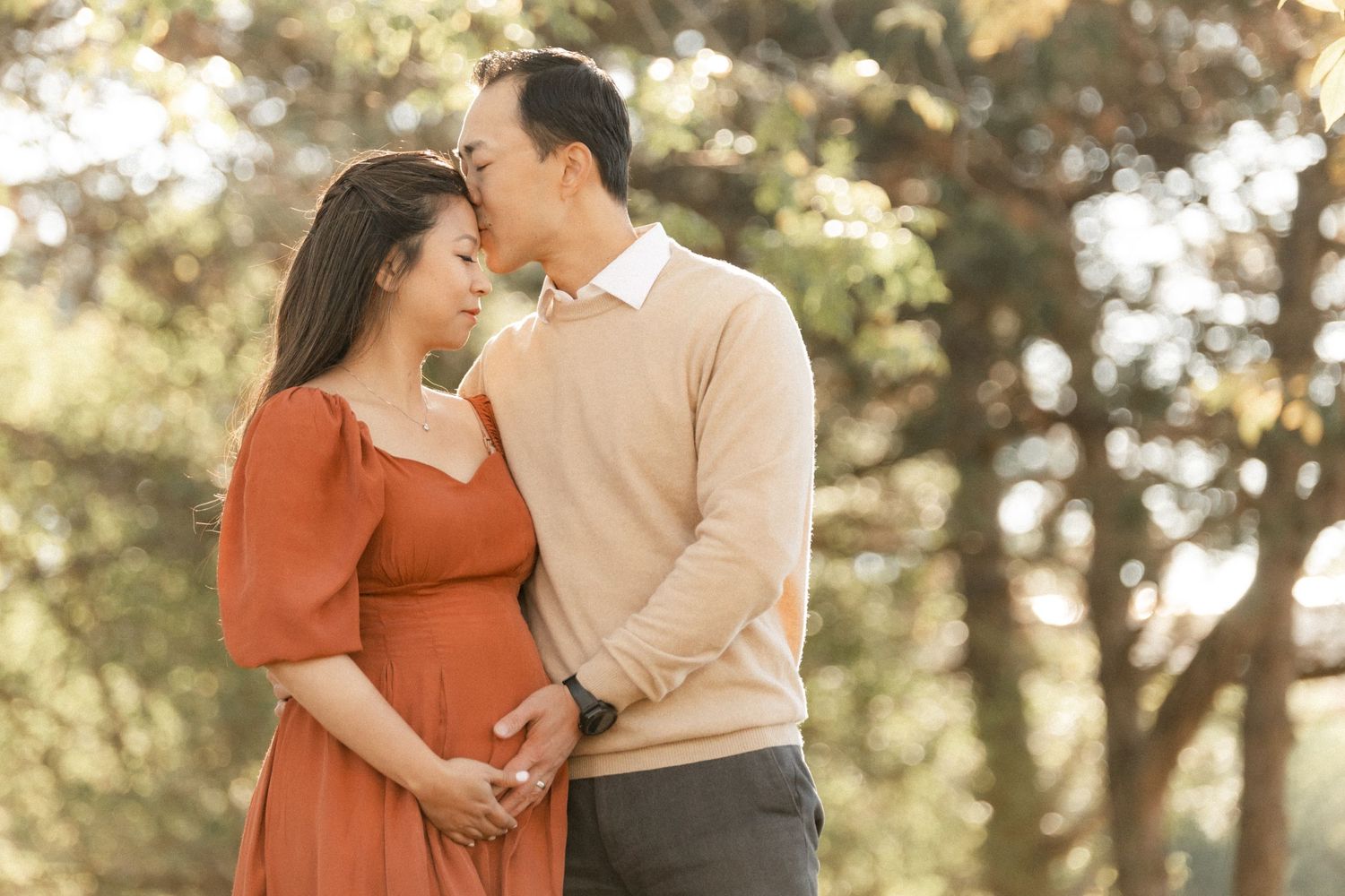 A romantic maternity photo shoot in nature with a couple in complimentary beige and rust colored outfits.