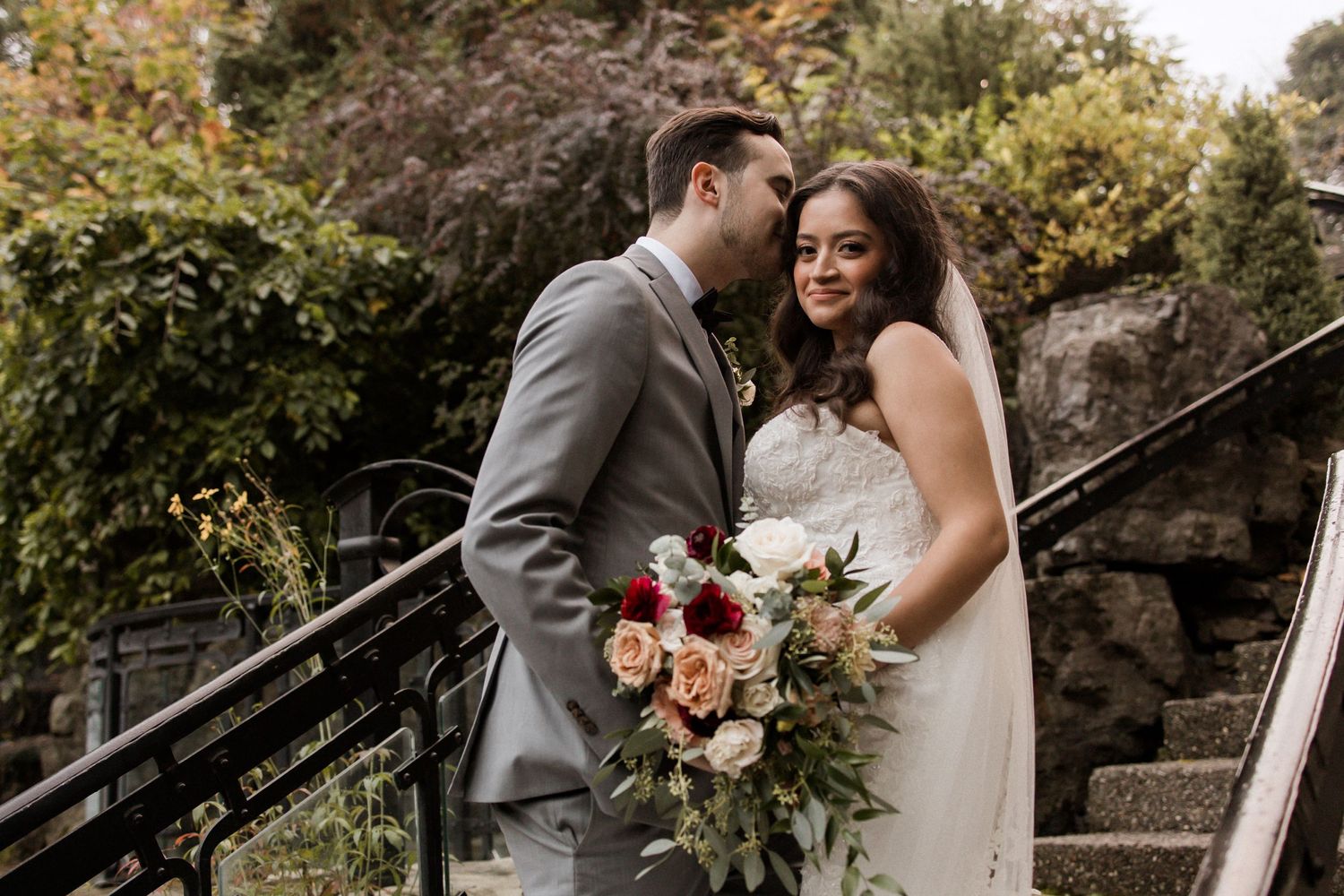 Happy newlyweds share candid moment on garden steps with autumn foliage.