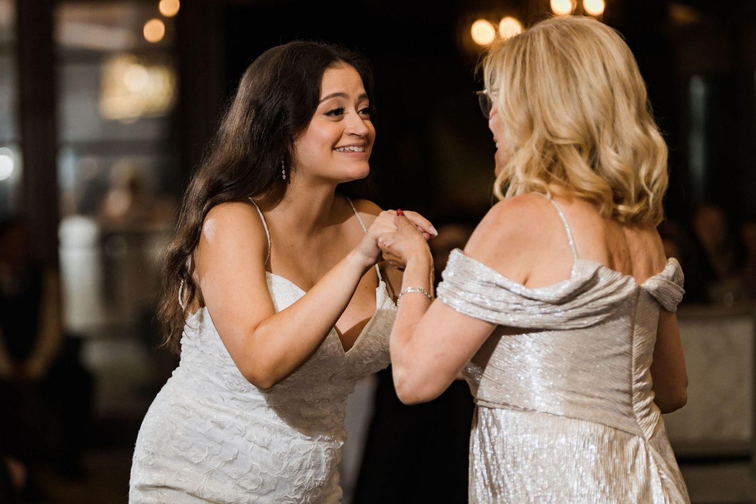 Two wedding guests in white dresses share a joyful moment together at an evening celebration.