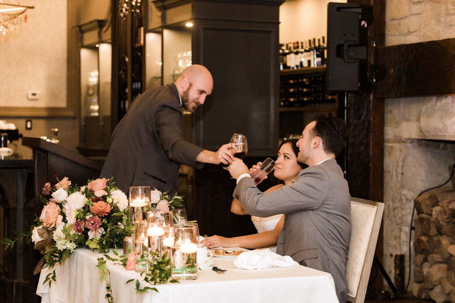 A person pours champagne for guests at an elegant dinner table with floral arrangements.