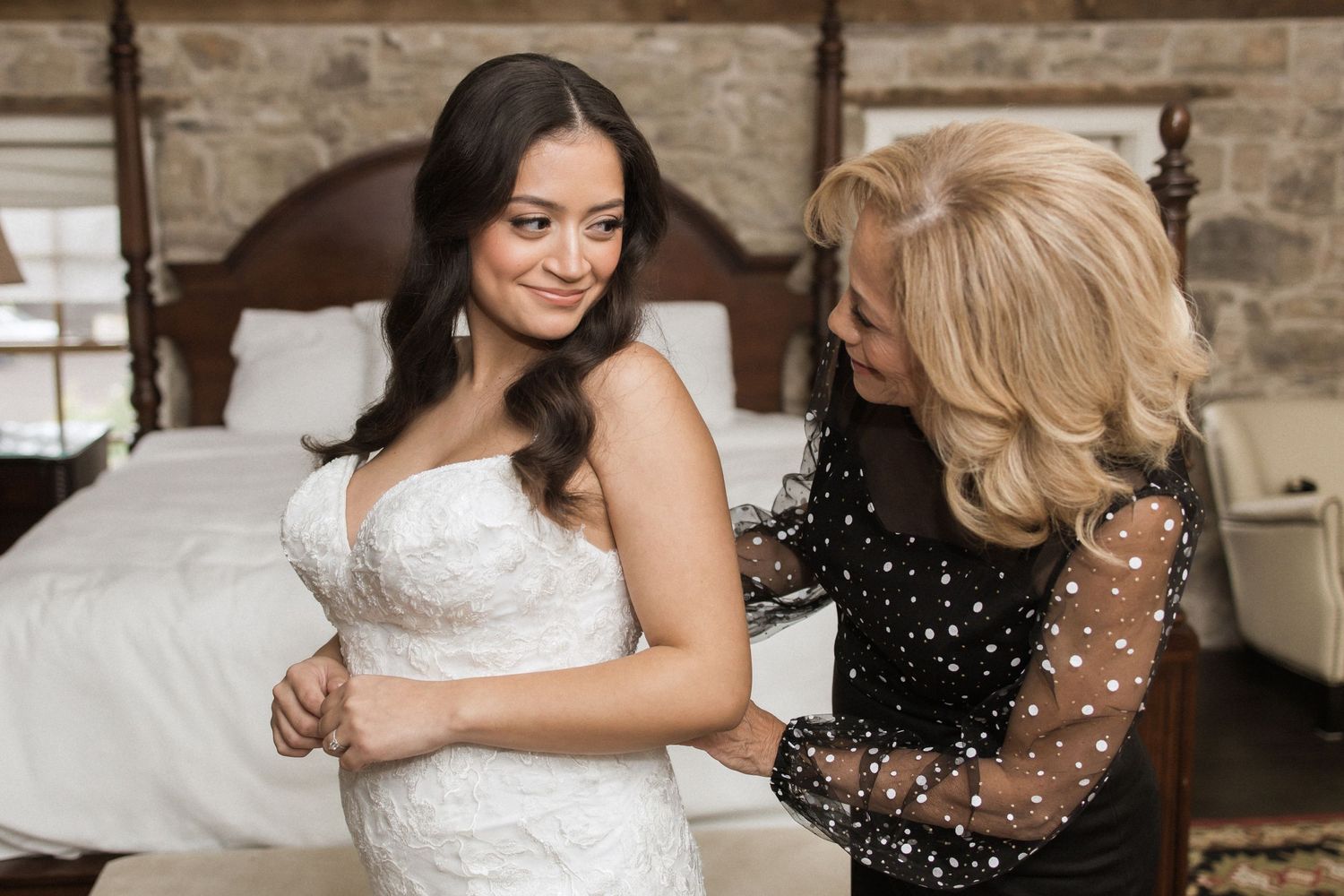 A bride in a white lace wedding dress gets help from someone wearing a black sparkly dress.