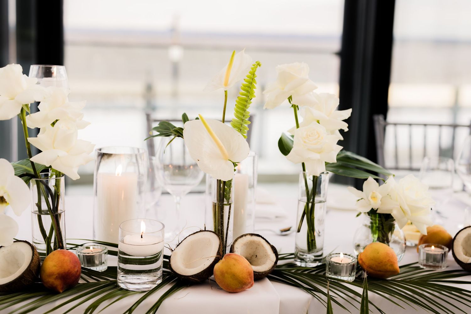 Tropical beach-themed table decor with white flowers, coconuts, and palm leaves.