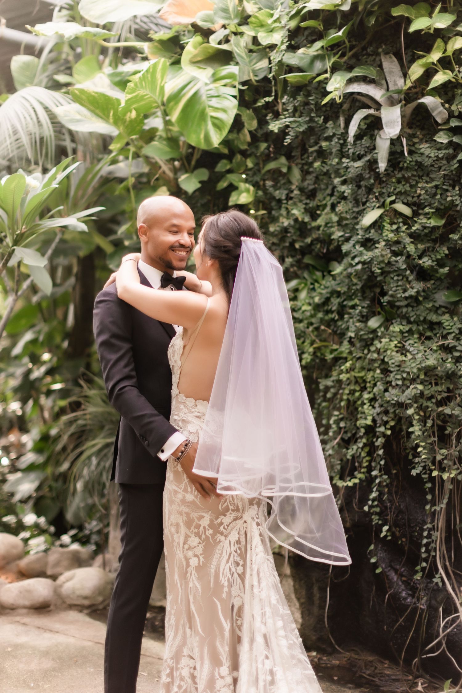 Romantic embrace between newlyweds in front of a tropical garden wall.