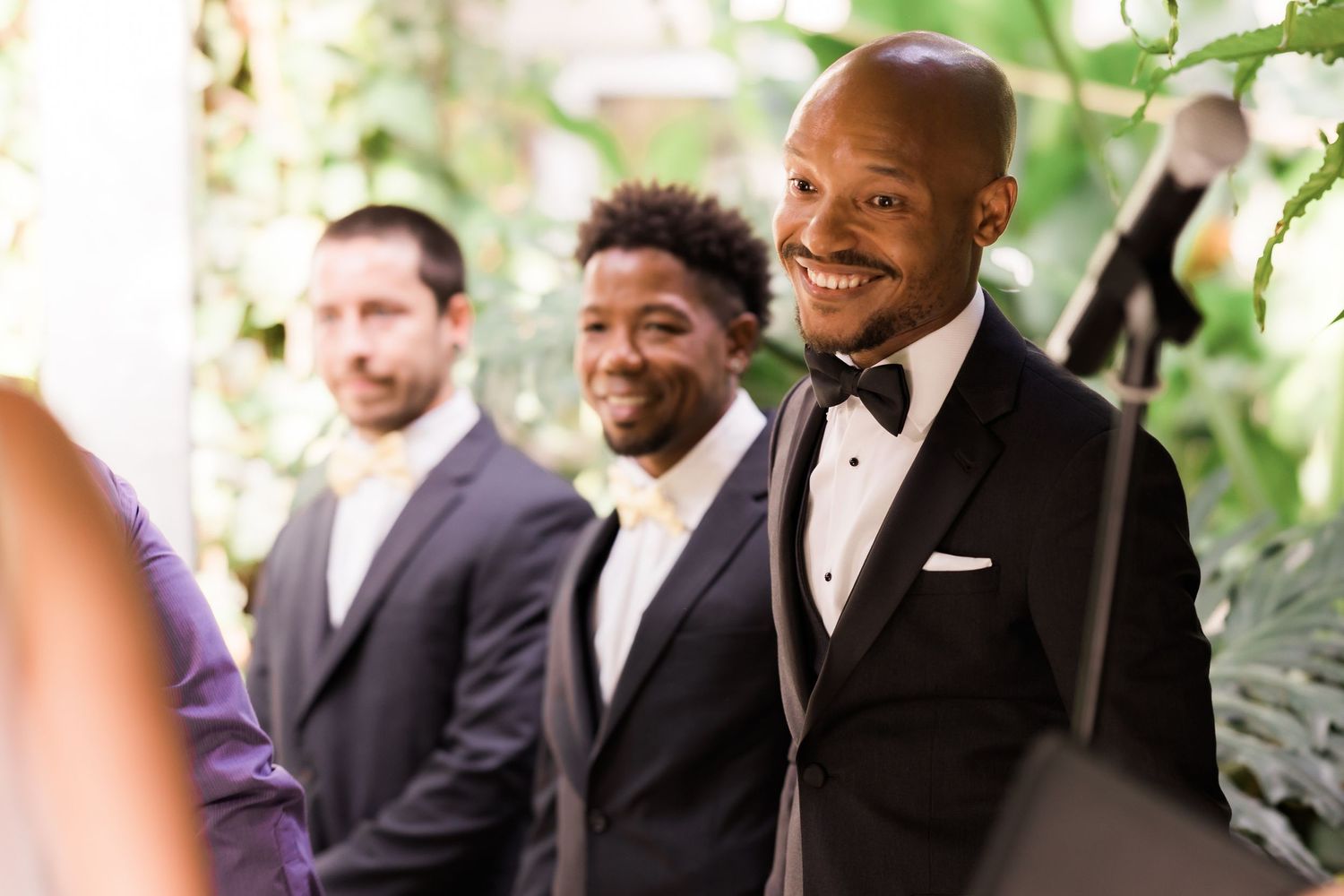 Wedding party members stand together smiling during an outdoor ceremony.