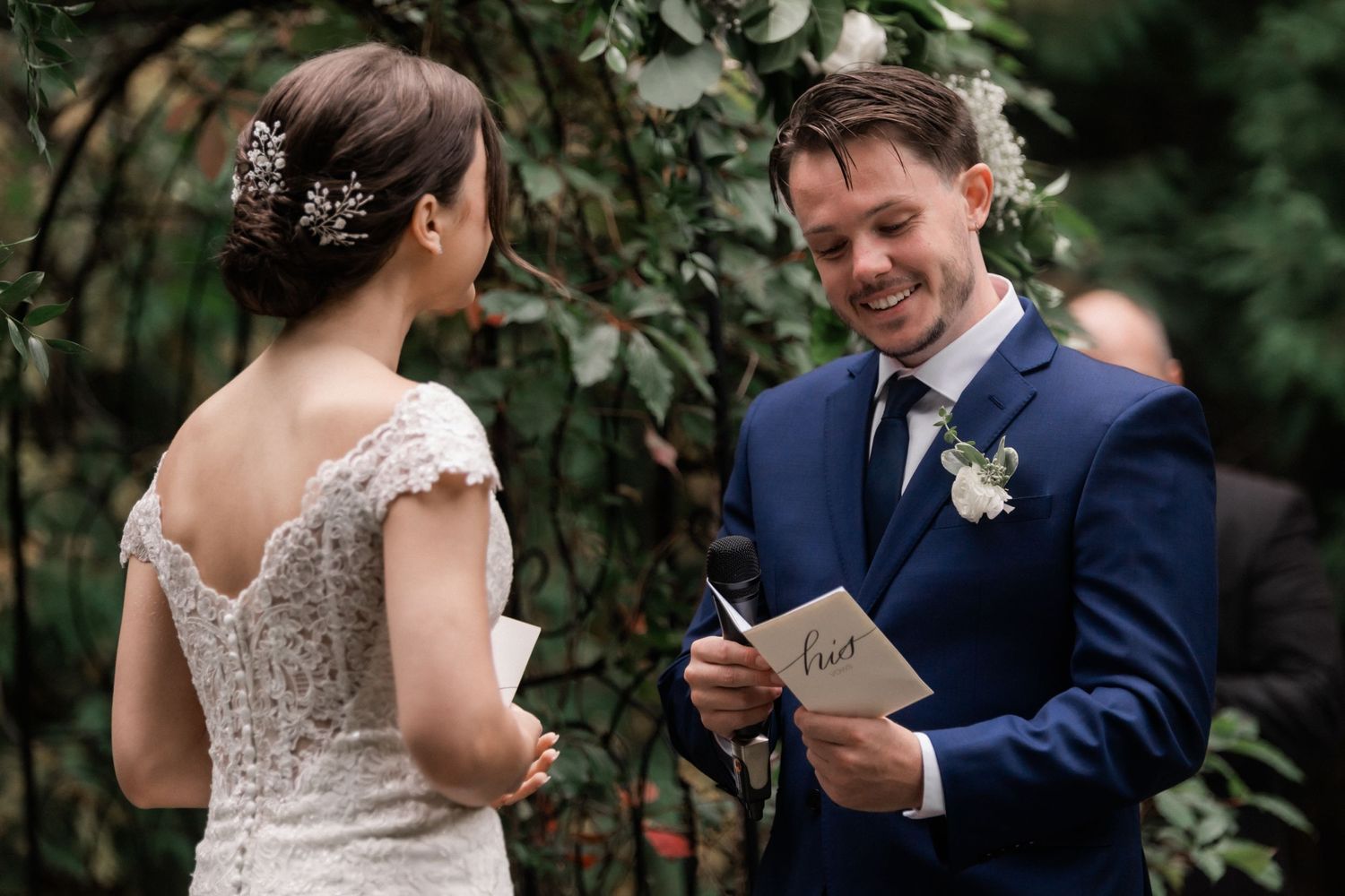 A couple shares lighthearted moments while reading vows surrounded by garden foliage.