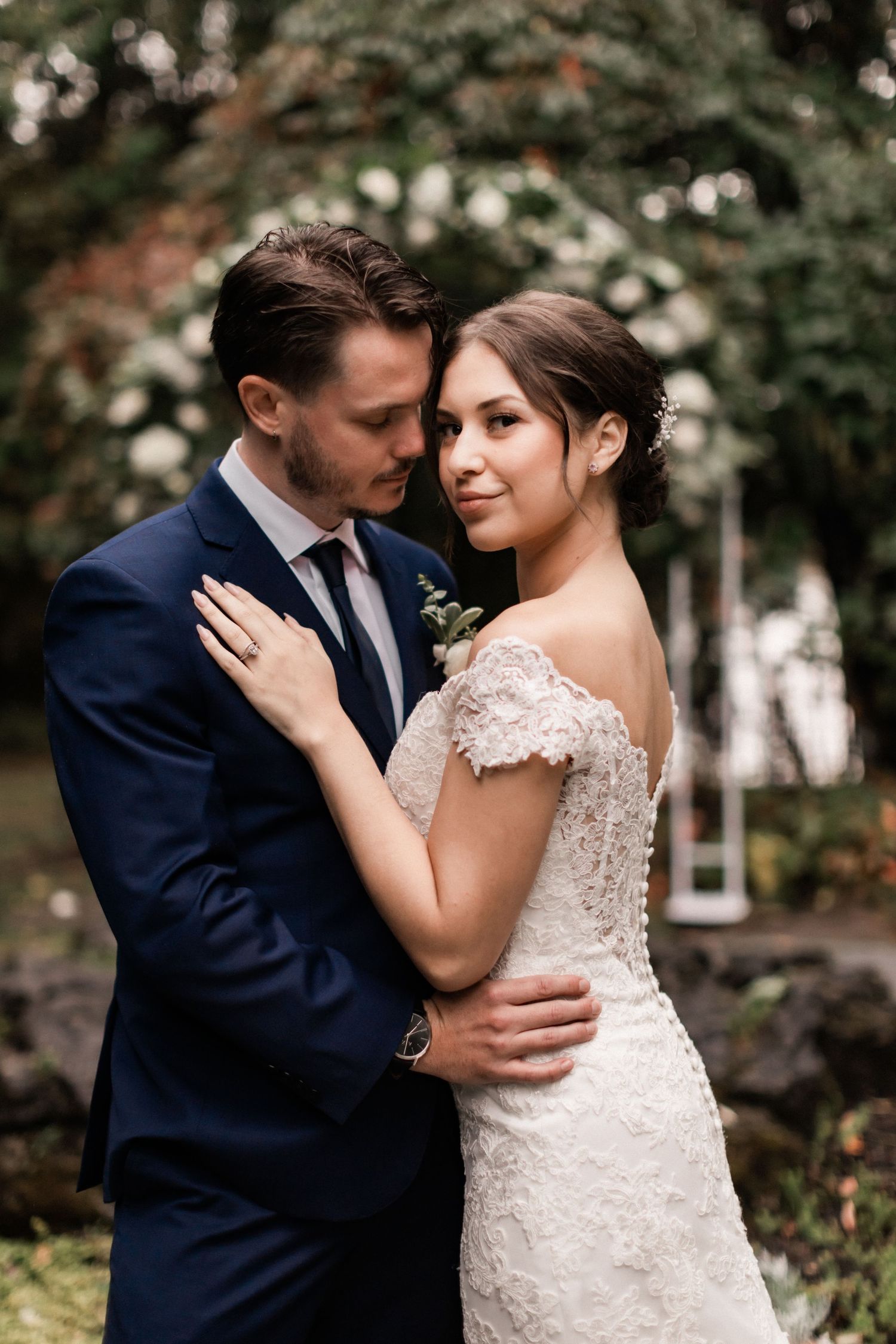 A romantic wedding portrait of a couple embracing outdoors with lush greenery in the background.