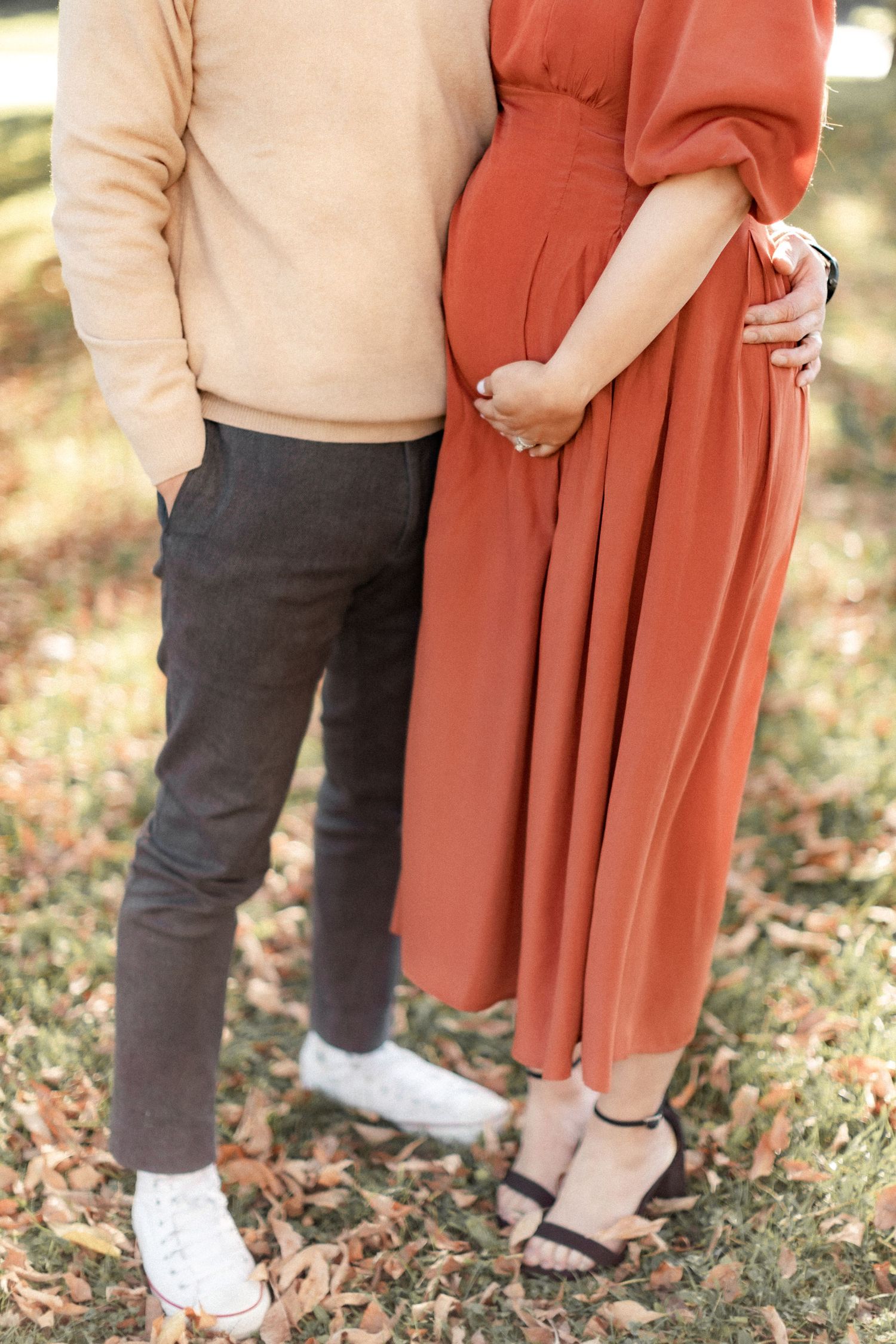 Cropped shot of couple standing close together highlighting maternity dress and casual attire.