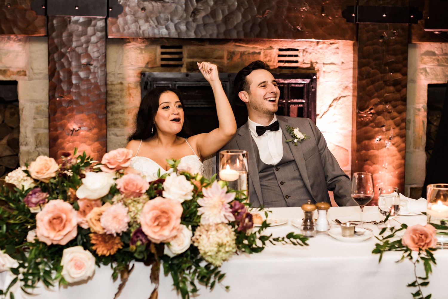 Couple at their wedding reception sharing joyful moment behind floral decorations.