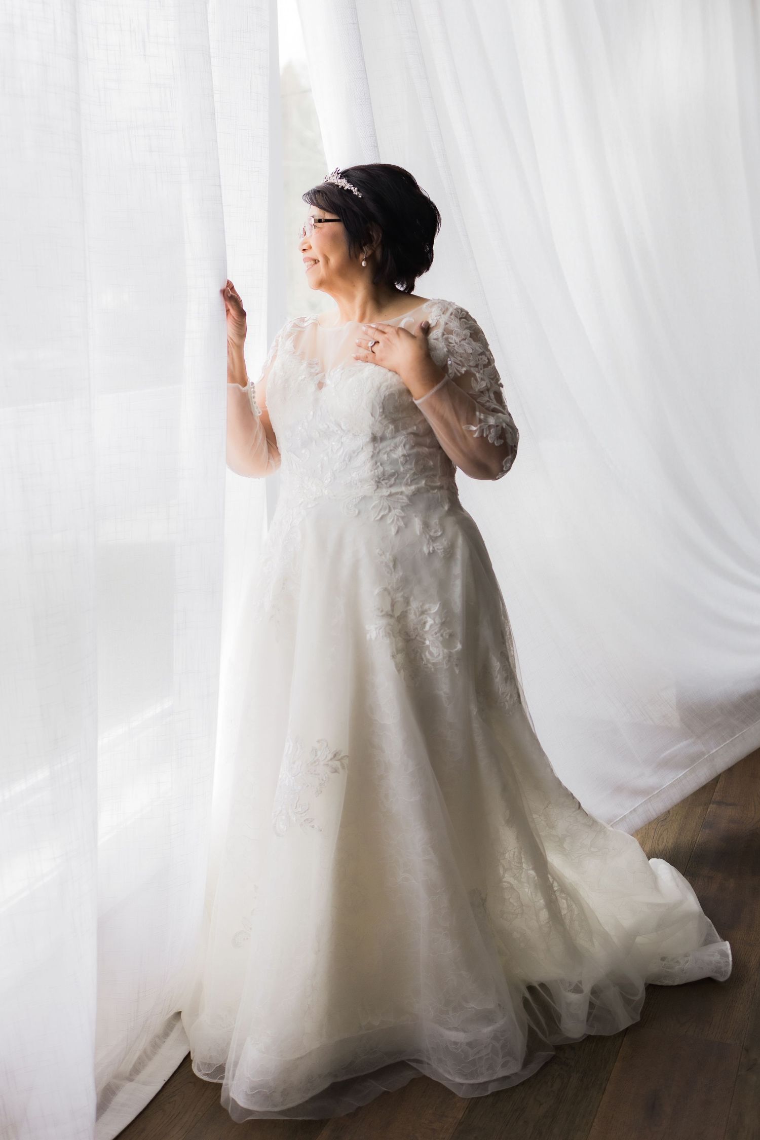 A beautiful lace wedding dress with long sleeves and delicate floral appliques photographed against a white backdrop.