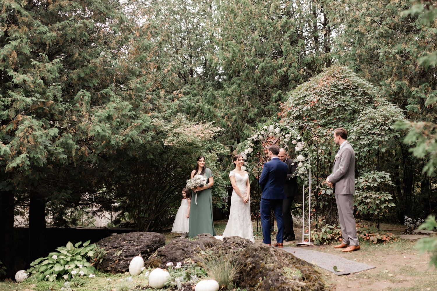 Intimate garden wedding ceremony with wedding party gathered under lush greenery.