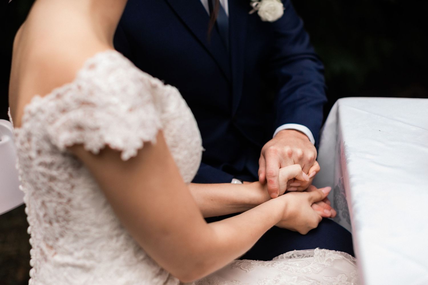Close-up detail of hands during wedding ring exchange at outdoor ceremony.