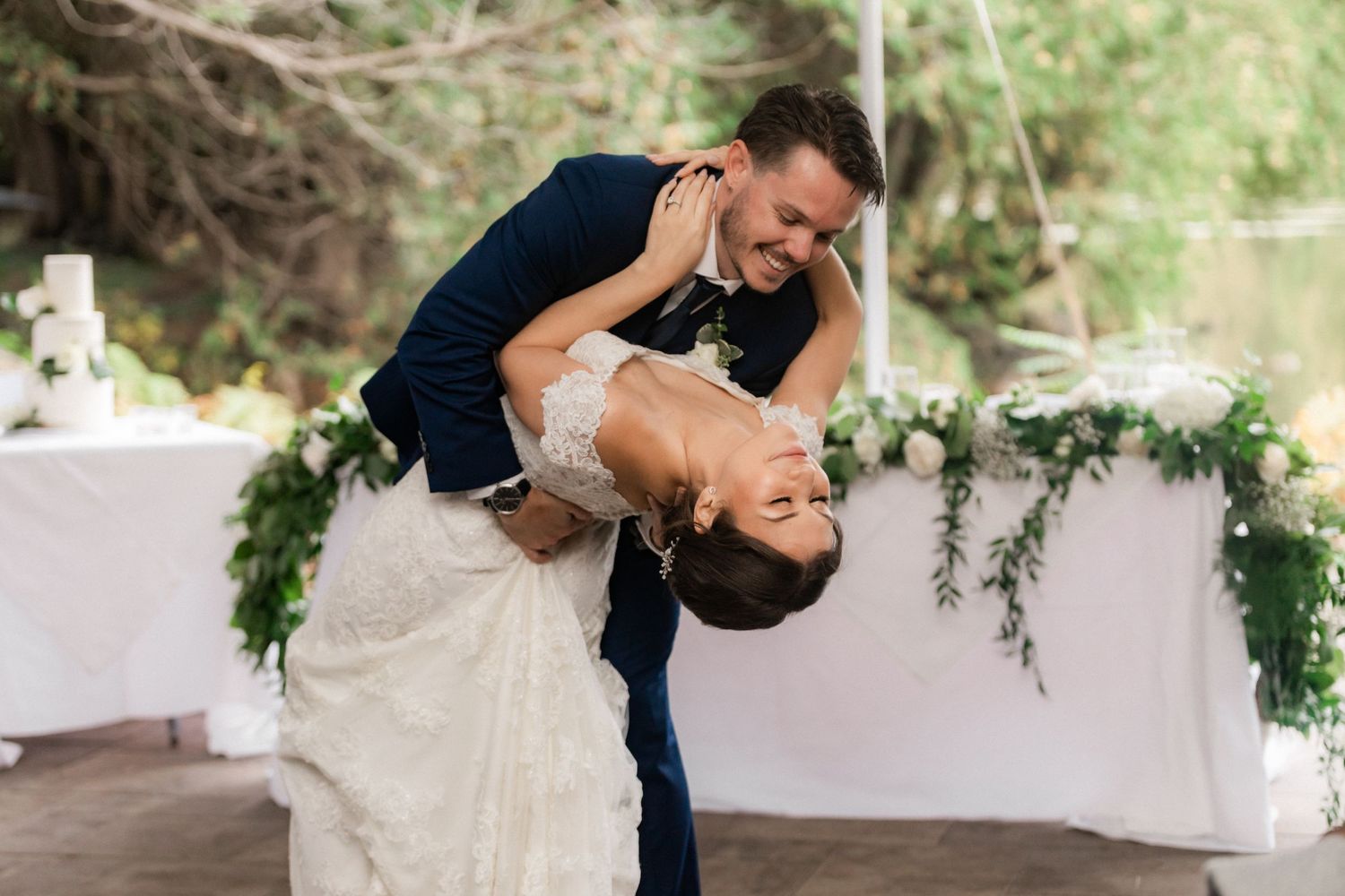 Couple performs dramatic dance dip during wedding reception outdoors.