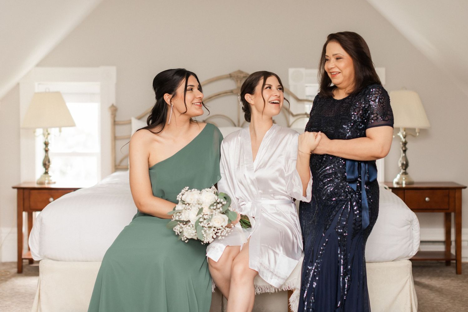 Wedding party in elegant dresses sitting together on white bed.