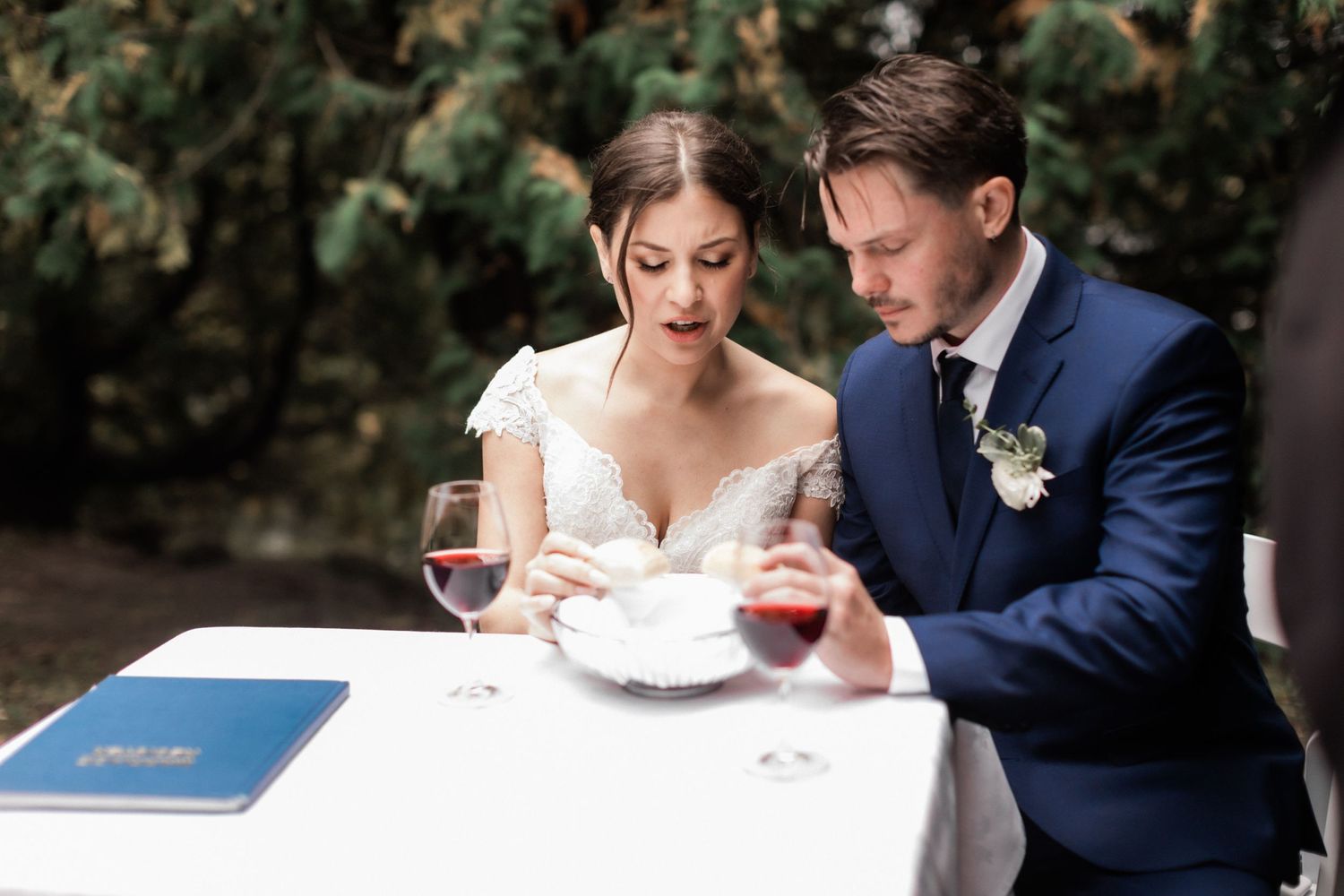 A couple shares a moment at their wedding reception table with wine glasses and paperwork.