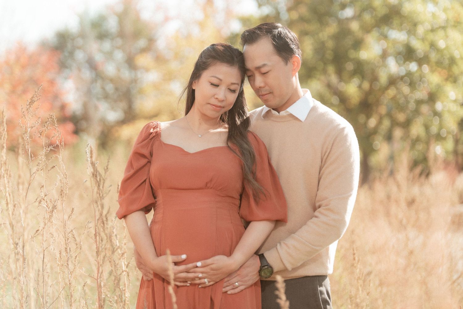 Romantic maternity photo of couple embracing in sunlit meadow with tall grass.
