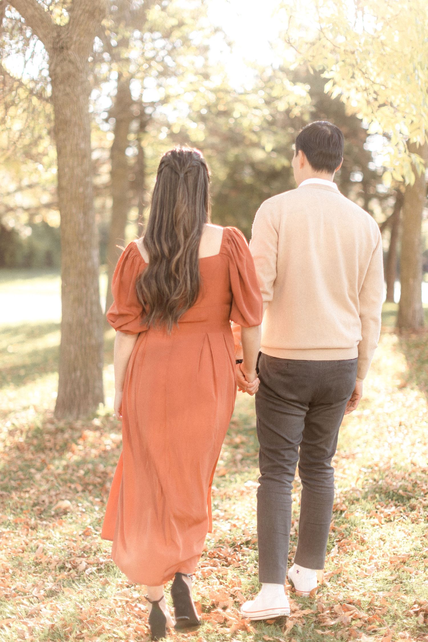 Back view of couple walking together through sunlit autumn park.