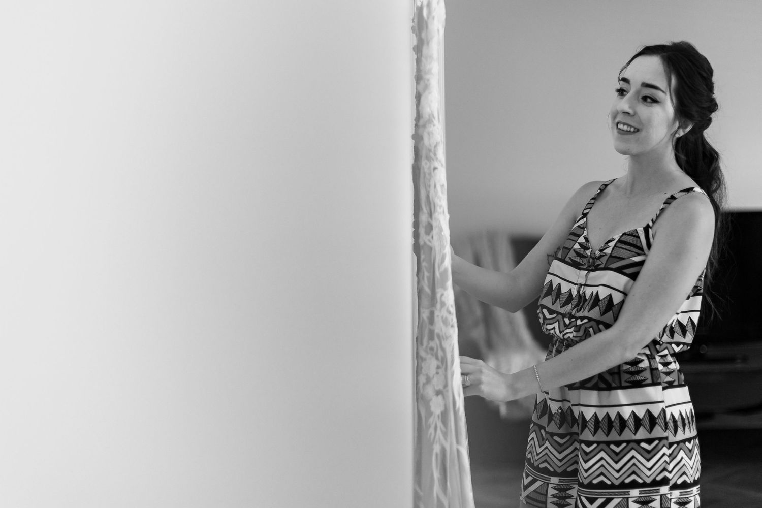 Black and white image of person in patterned dress looking at wedding gown.