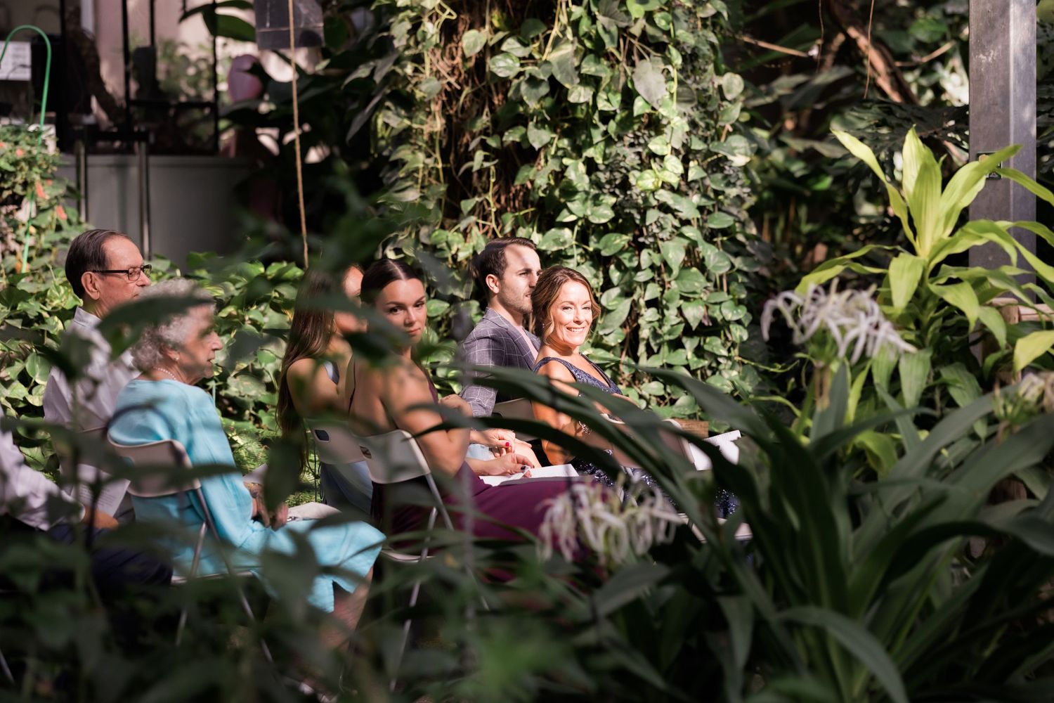 Guests seated in a lush greenhouse environment surrounded by tropical plants.