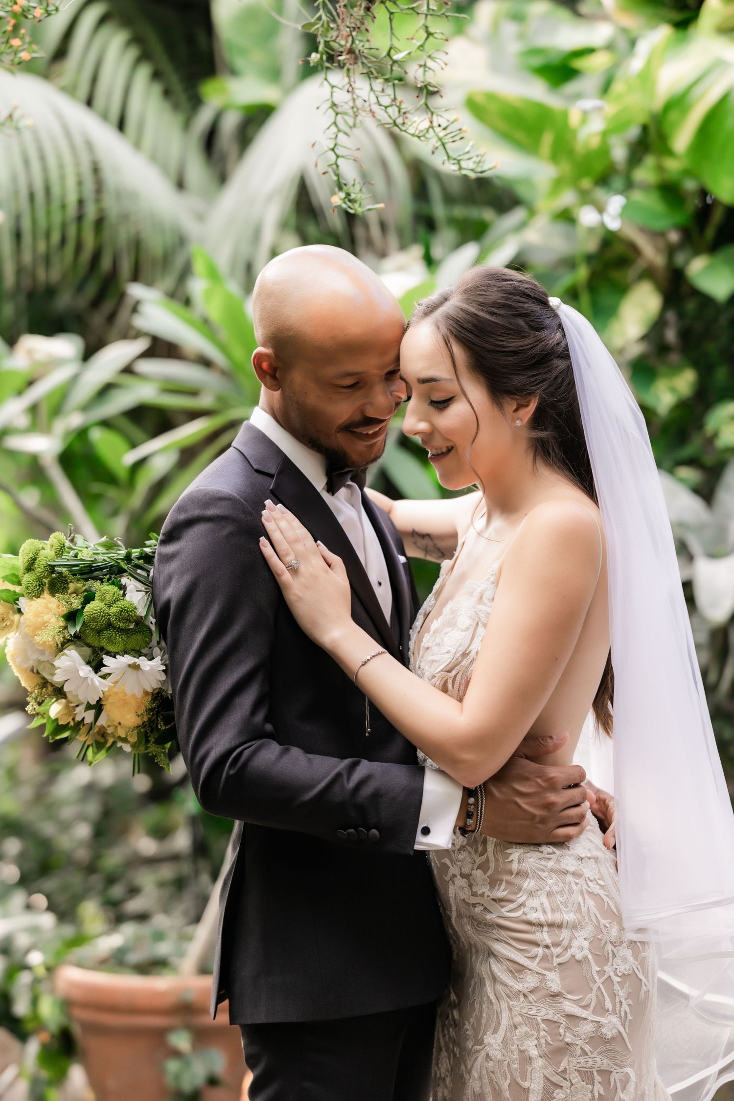 Wedding couple sharing an intimate moment in a botanical garden setting with tropical backdrop.