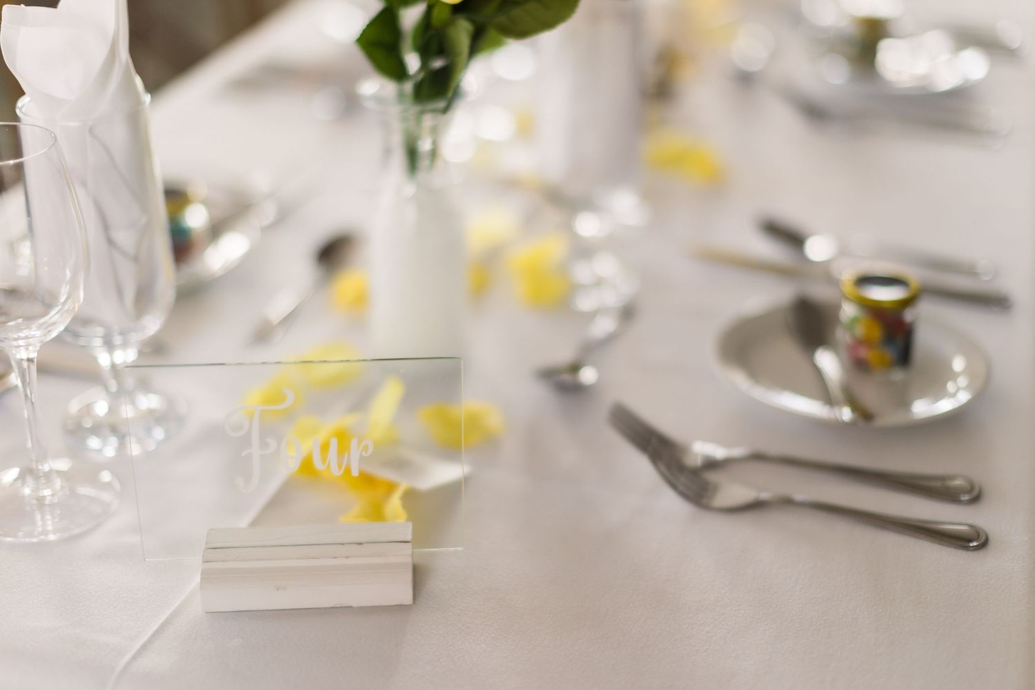 Wedding table setting detail with scattered yellow petals and wine glasses.