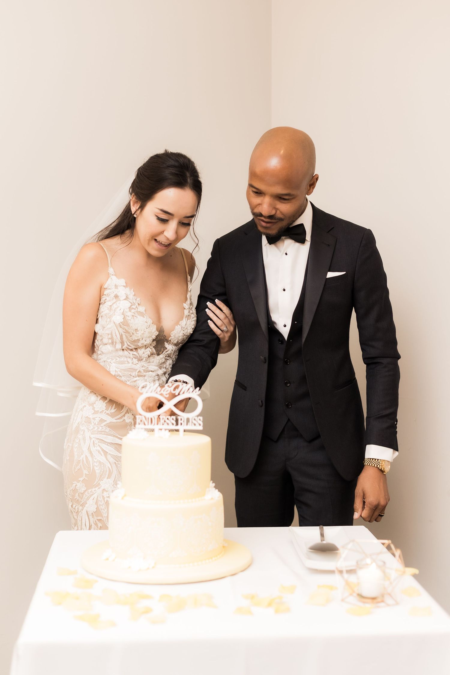 Newlyweds stand together admiring their elegant white wedding cake.