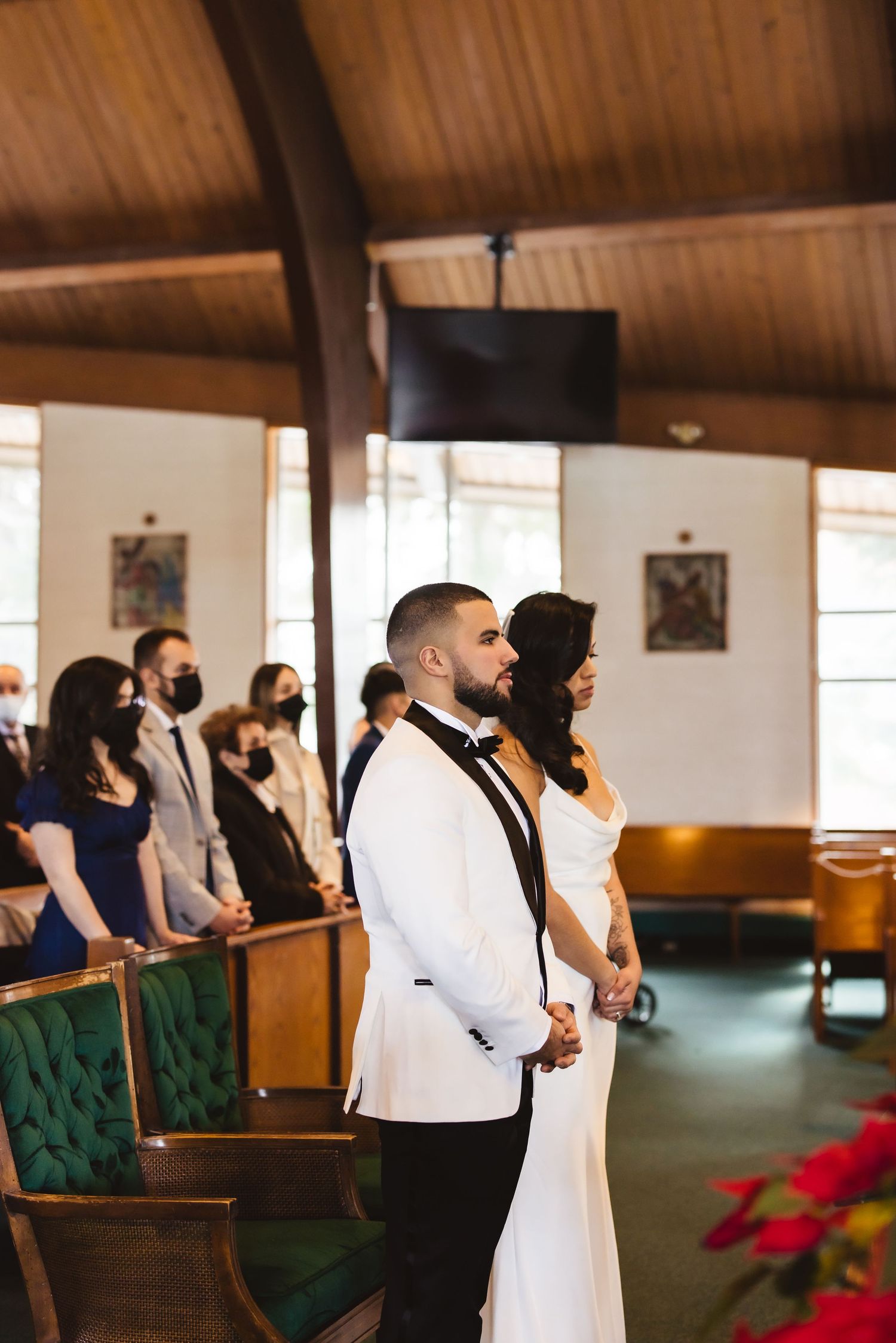 Wedding guests stand in church pews during a ceremony with wooden beamed ceiling.