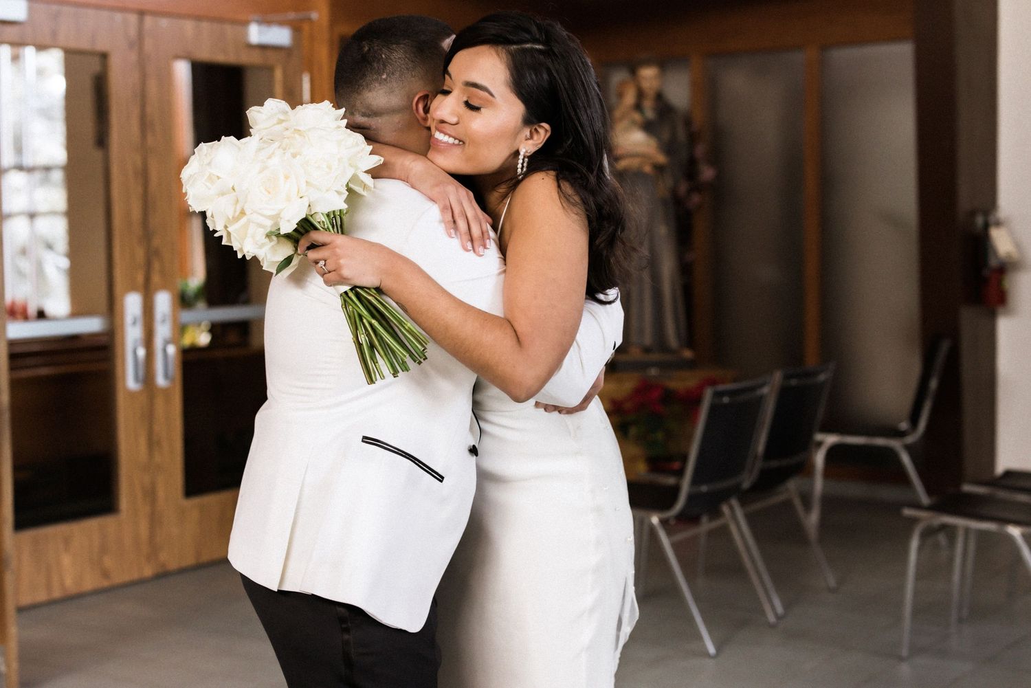 Newlyweds embrace while holding white flower bouquet during intimate wedding moment.