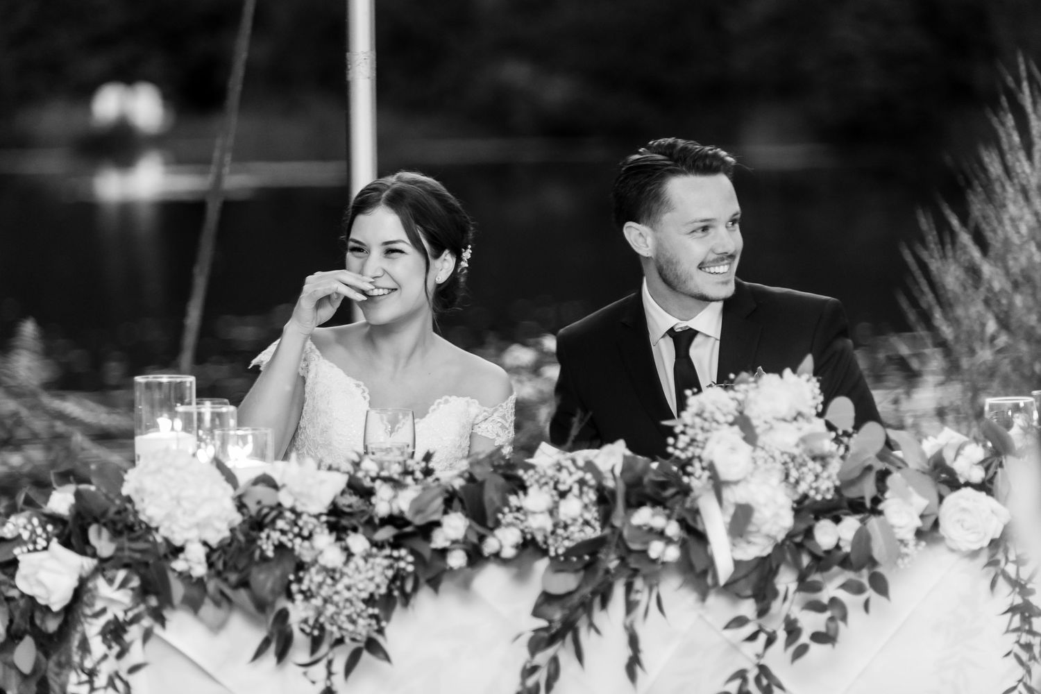 Newlyweds sit at their reception table adorned with elegant floral arrangements and share a joyful moment.