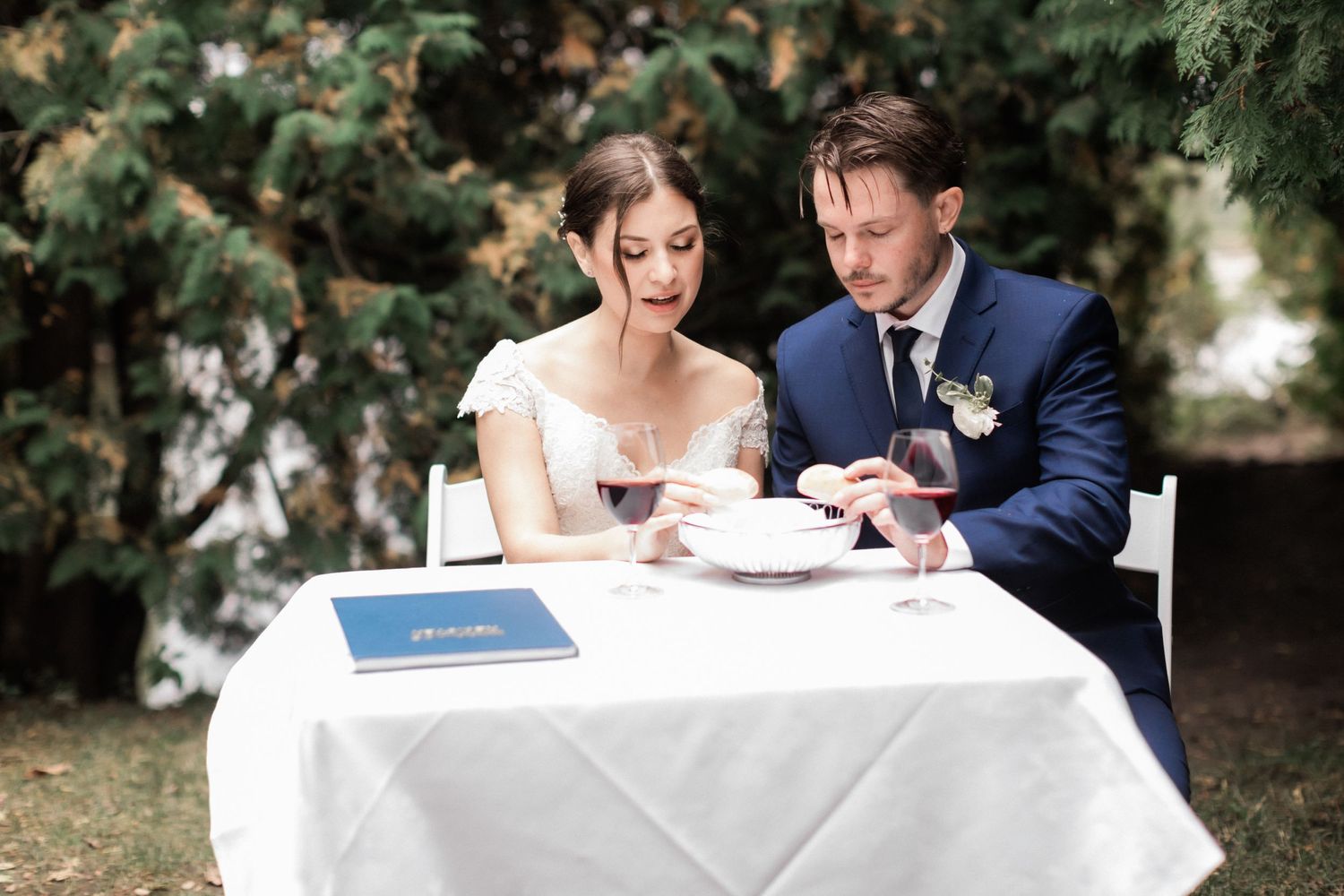 A couple shares a joyful moment while signing documents at a white-clothed table outdoors.
