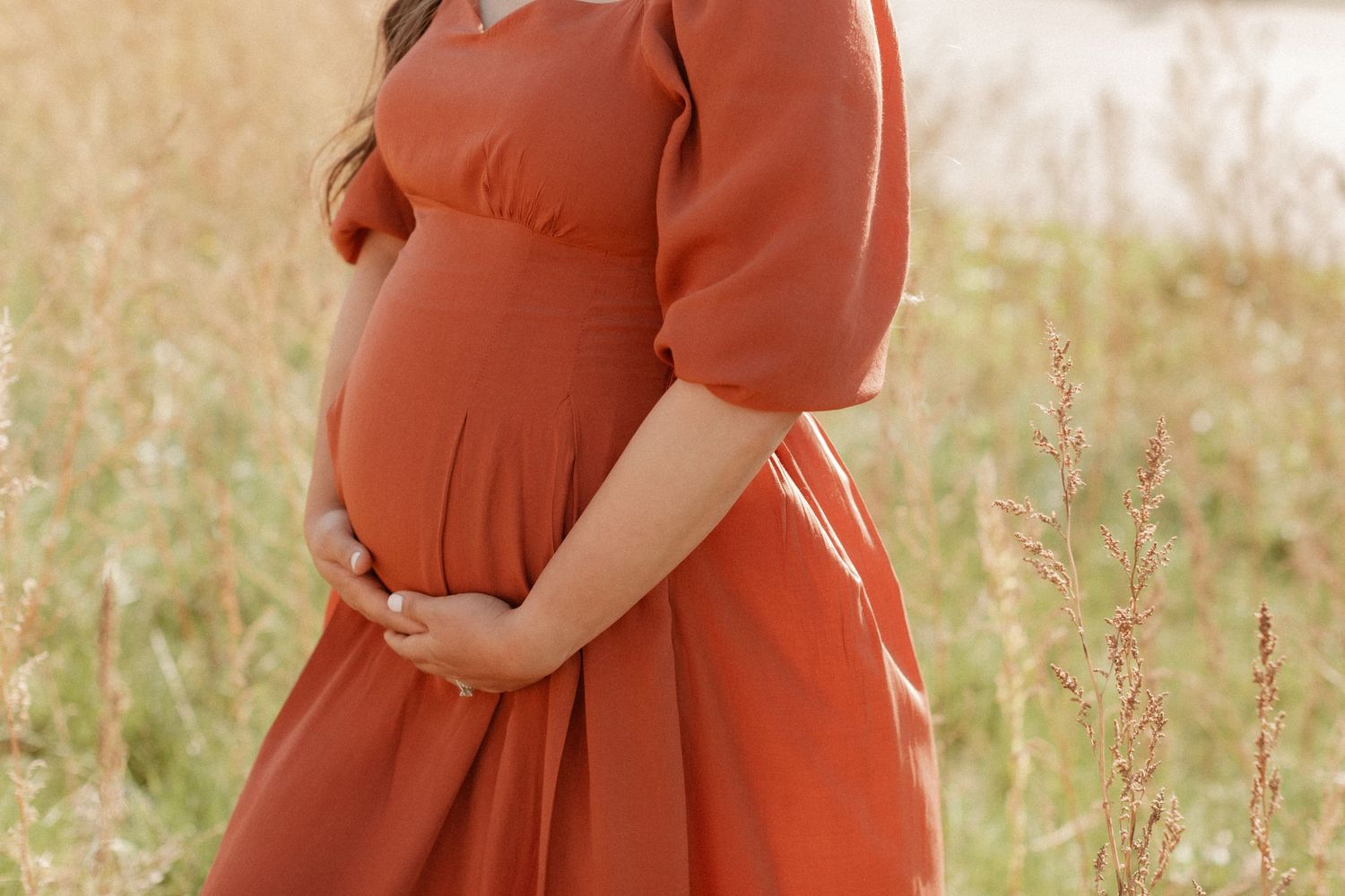 Side profile of pregnant woman in rust-colored dress with puff sleeves.