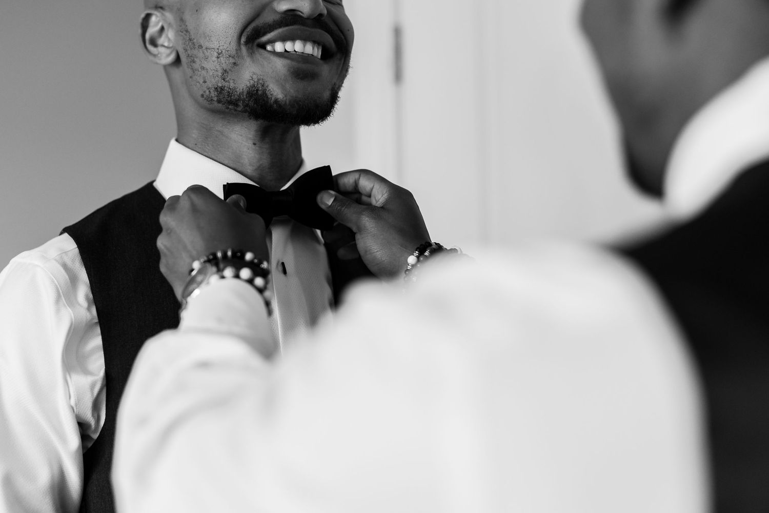 Close-up black and white shot of bow tie adjustment during wedding preparations.