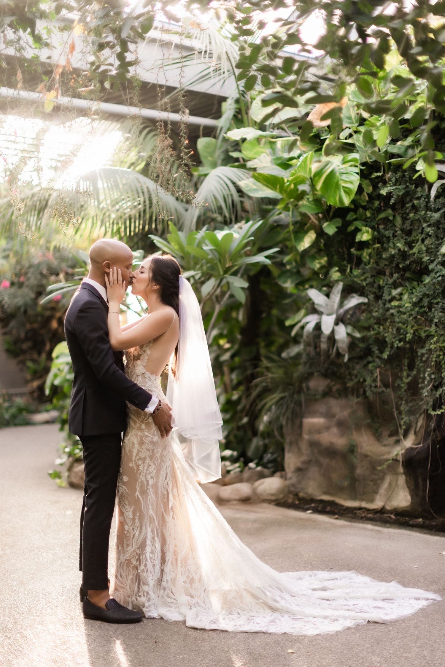 A couple embraces in a romantic garden setting wearing elegant wedding attire.