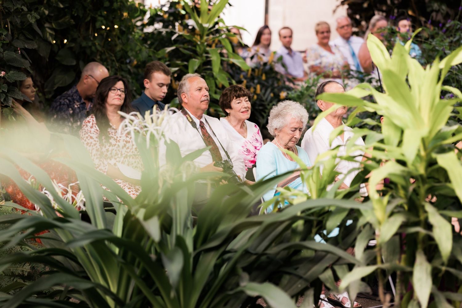 Wedding guests seated among lush tropical garden foliage during ceremony.