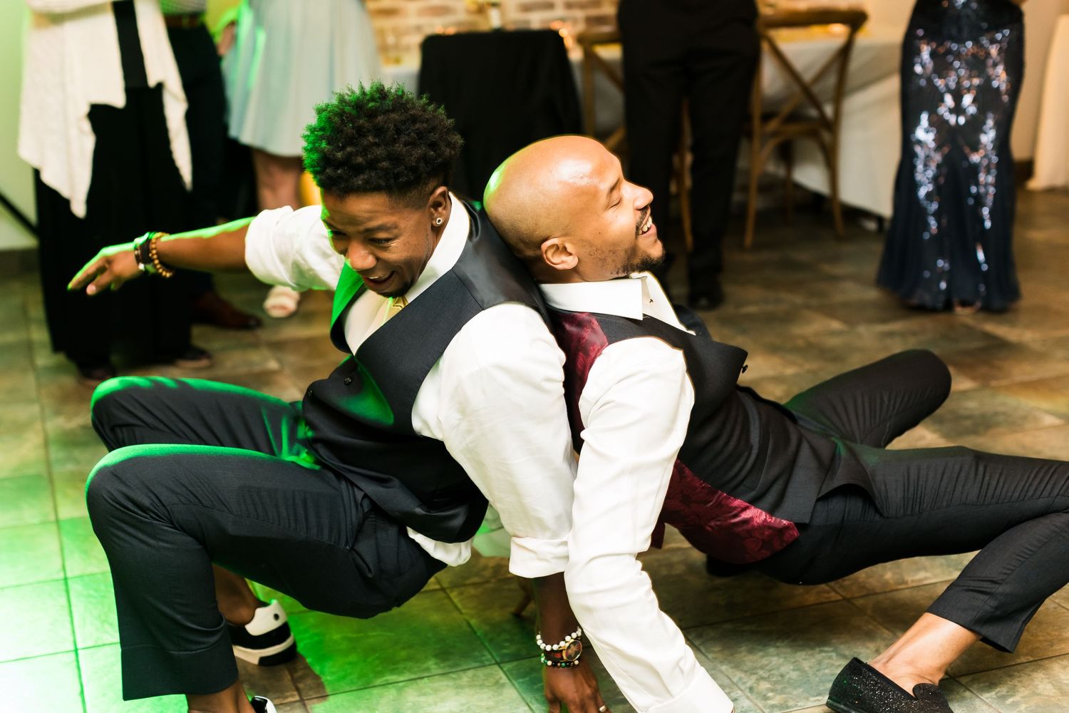 Wedding guests perform energetic dance moves on the reception floor with dramatic poses.