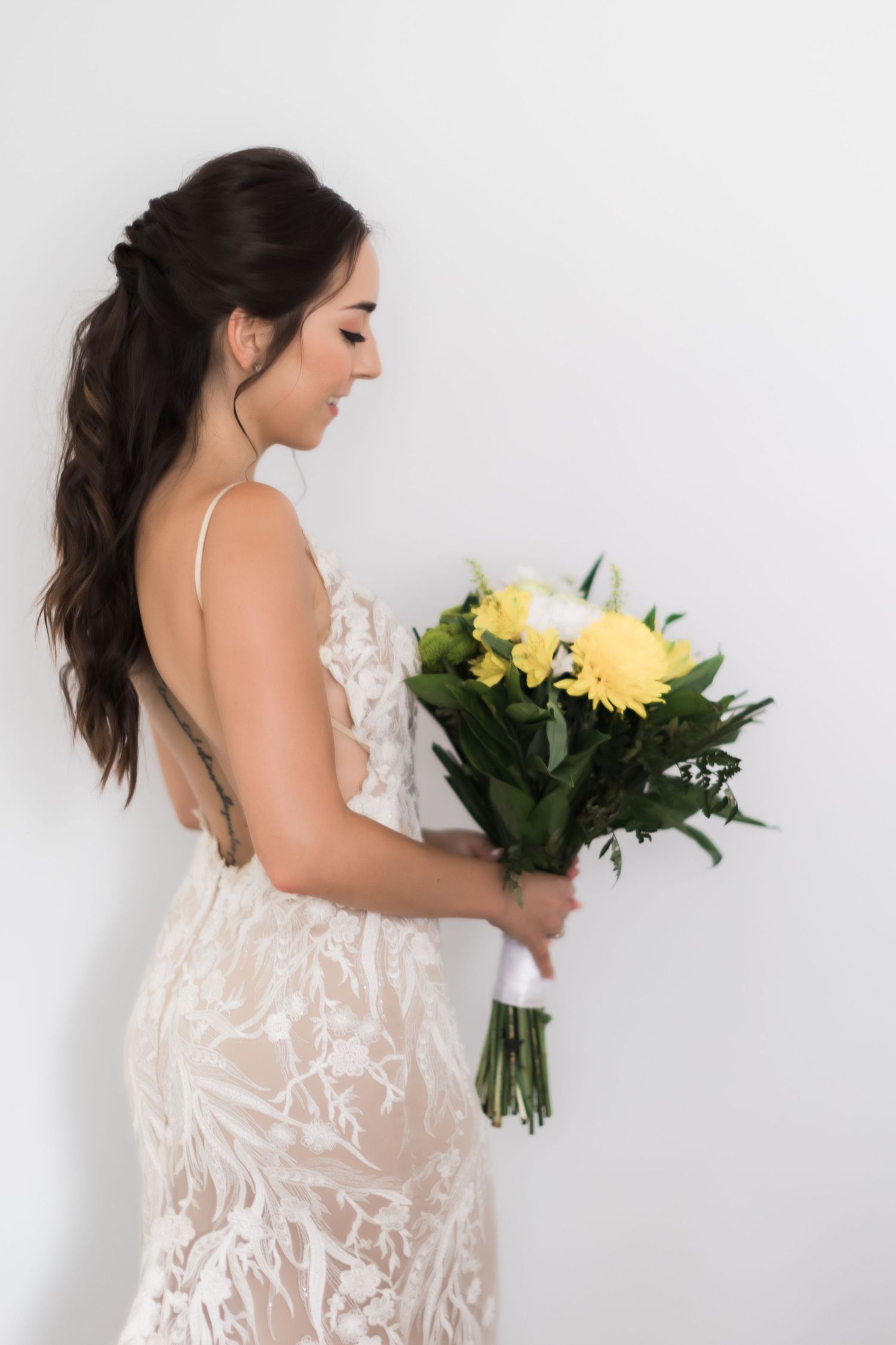Side view of bride holding yellow gerbera daisy bouquet in an elegant lace wedding dress.