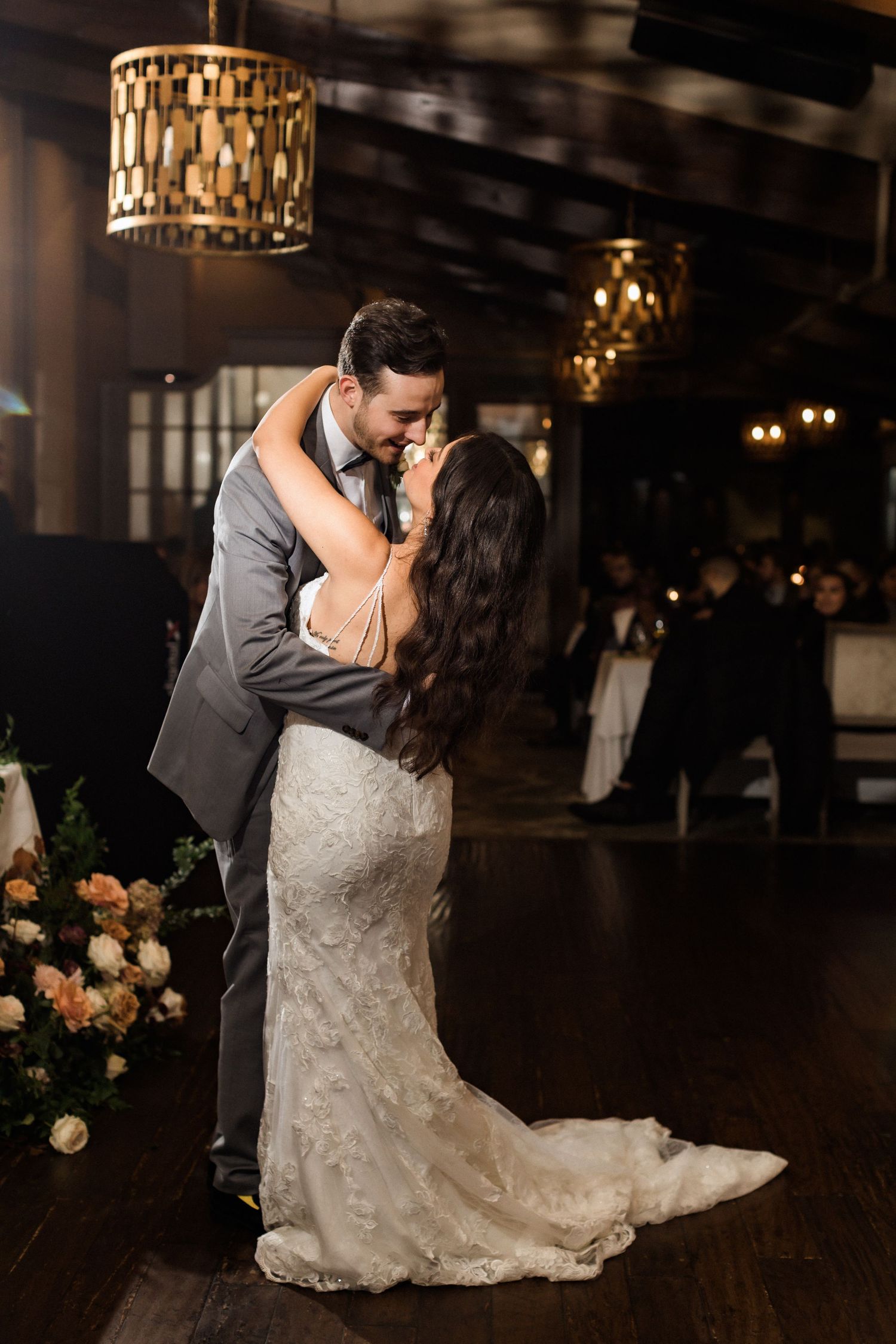 A romantic moment between newlyweds dancing under golden pendant lights.