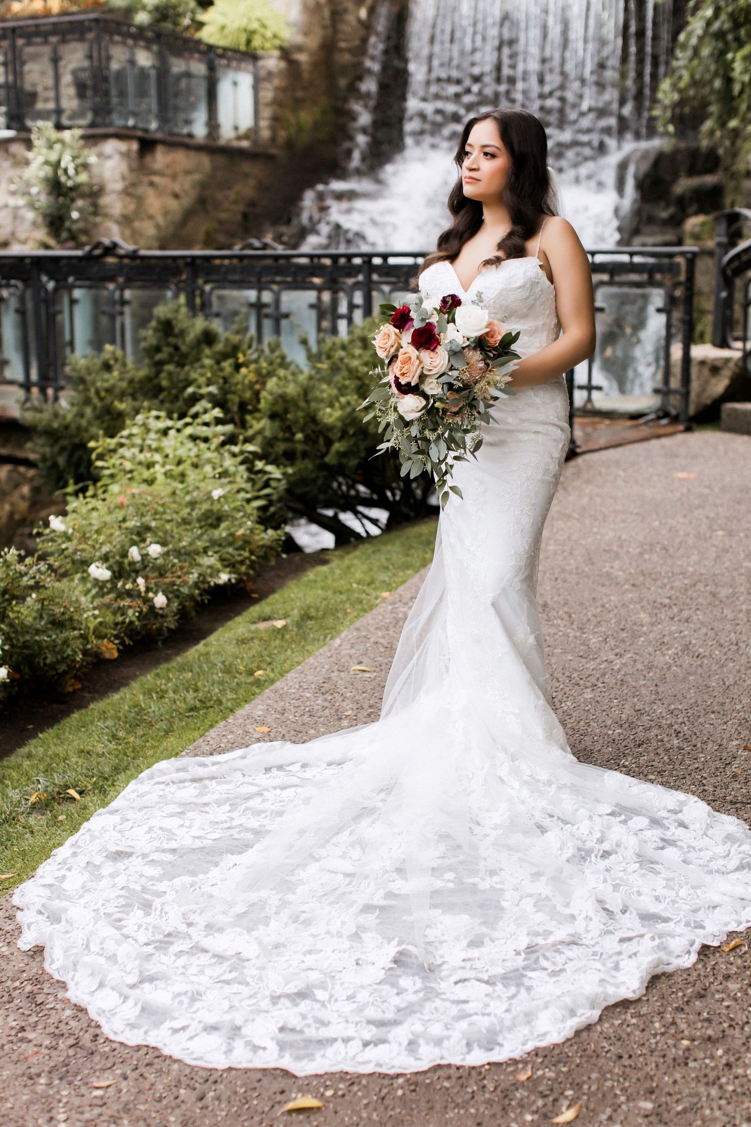 Stunning wedding portrait showcasing intricate lace train and garden waterfall scenery.