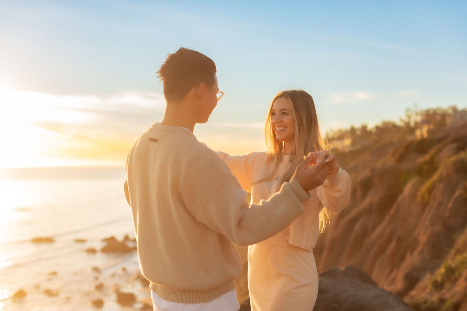 Couple sharing romantic moment on cliff overlooking ocean at sunset.