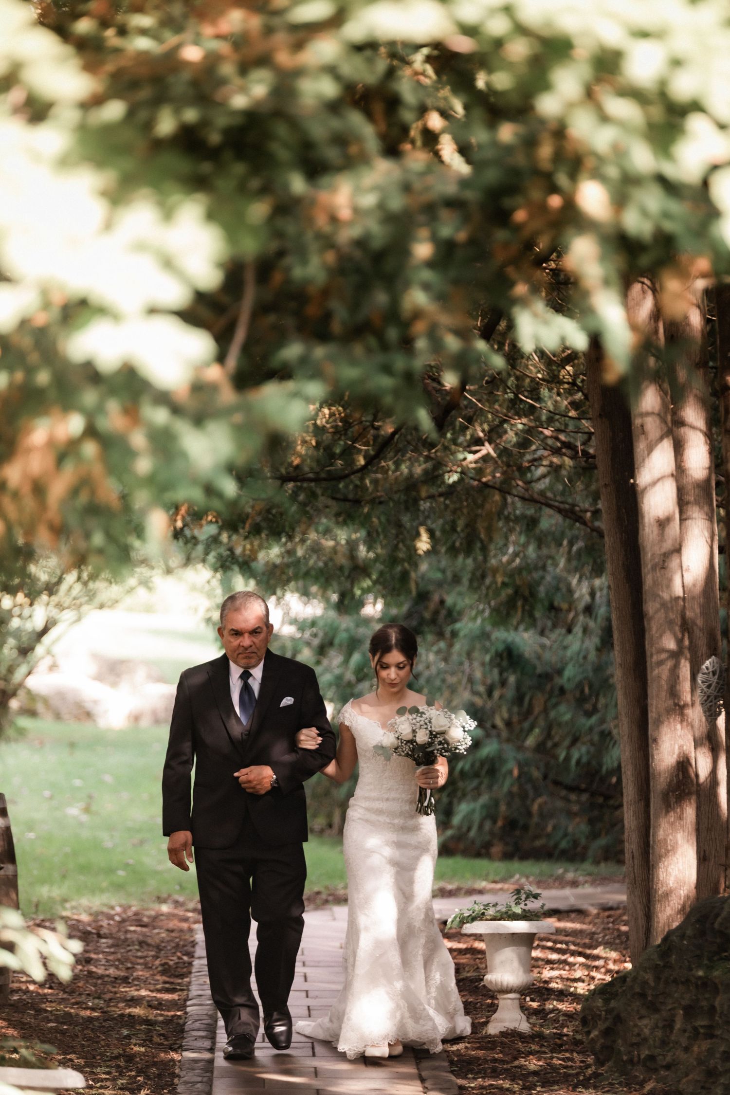 Wedding processional along tree-lined path during outdoor autumn ceremony.