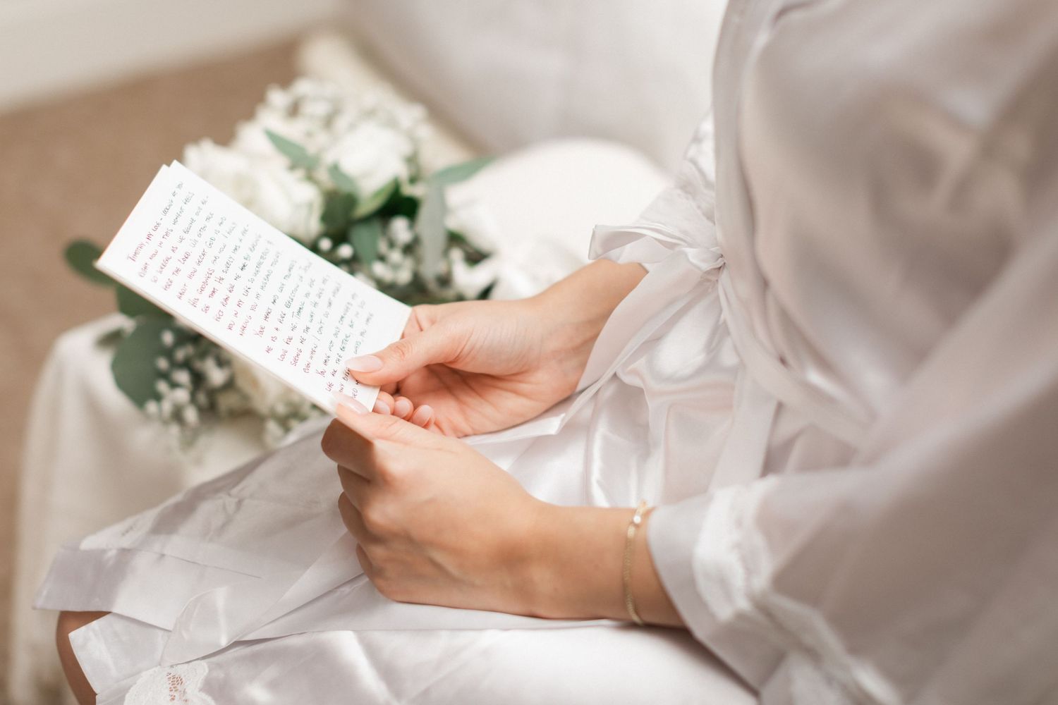 Close-up of hands holding wedding vows with white flowers in background.