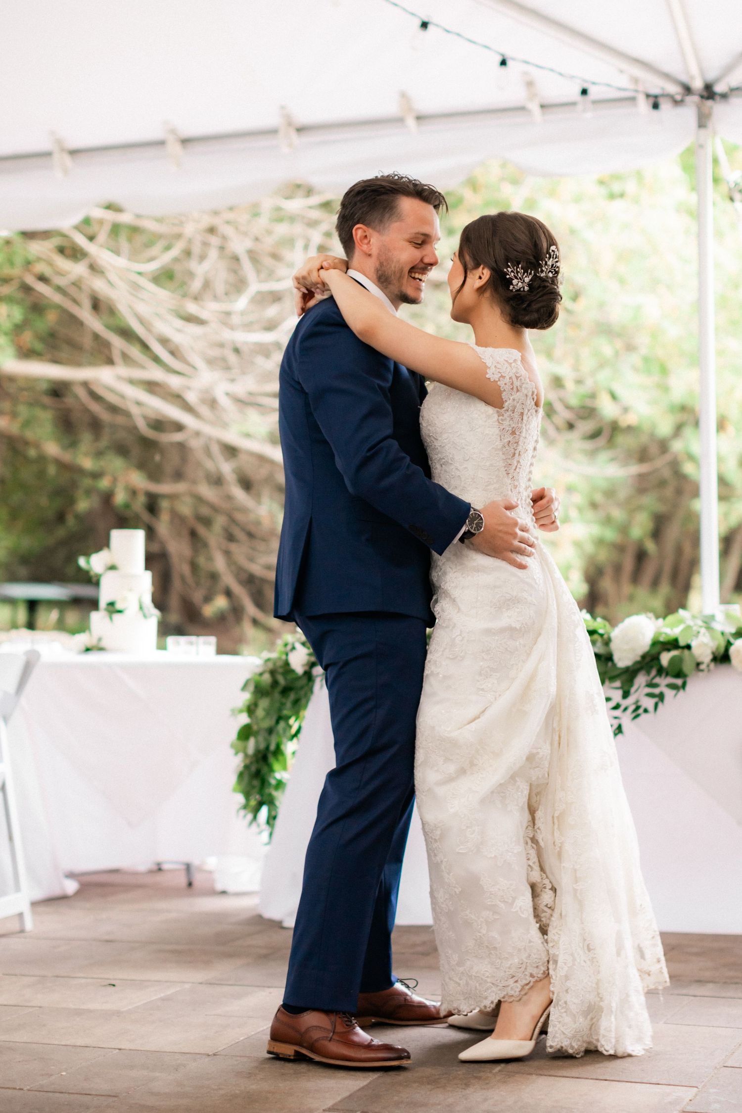 A romantic first dance moment under a white tent with elegant decor and greenery.