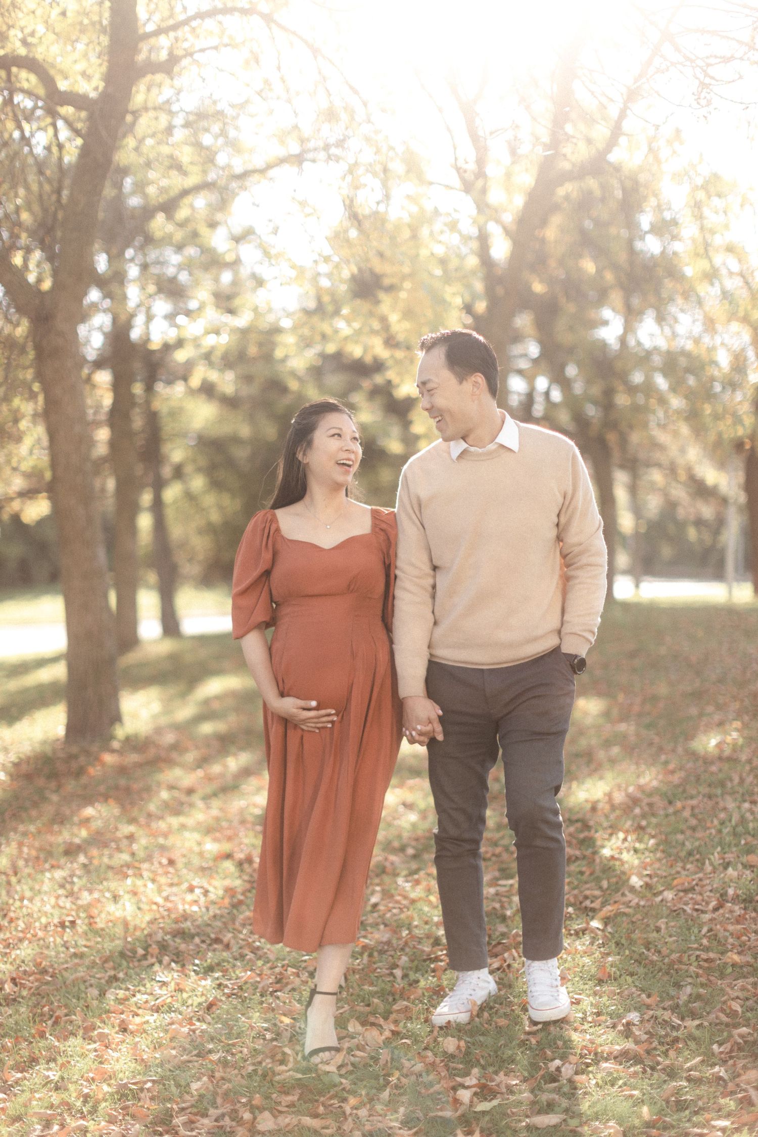 Expecting couple shares a loving moment while walking through a park on a sunny fall day.